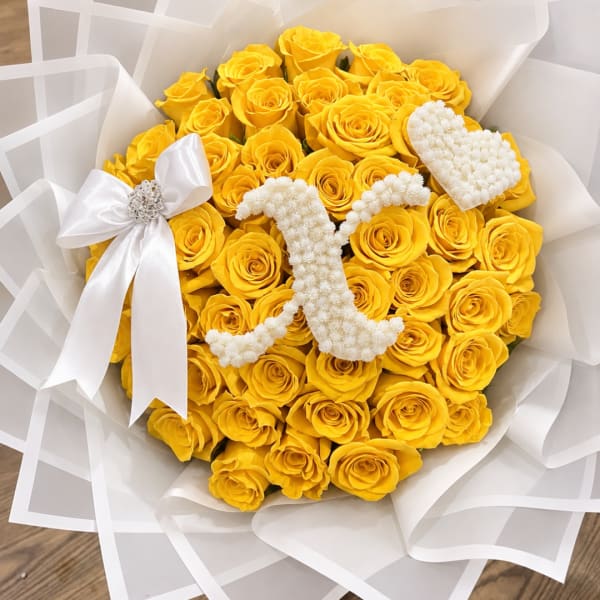 Bouquet of yellow roses with white floral heart accents and a white ribbon