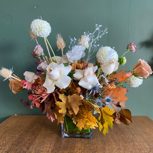 Mixed floral arrangement in a square glass vase with autumn leaves