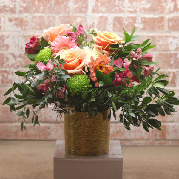 Mixed bouquet of peach and pink flowers in a gold vase