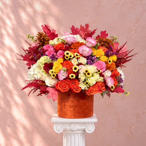 Large mixed bouquet in an orange vase on a white pedestal