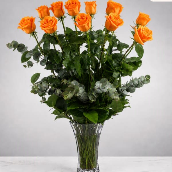Orange roses arranged in a clear glass vase with mixed greenery
