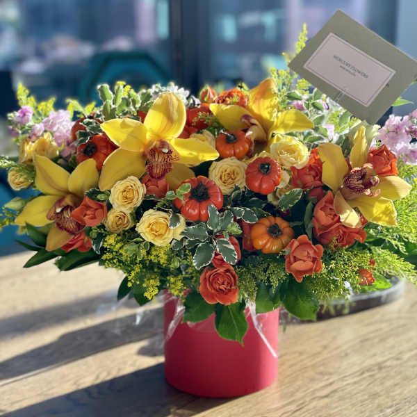 Bright mixed flower arrangement in a pink vase with yellow orchids and roses
