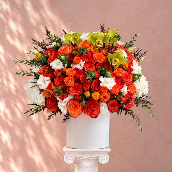 Large orange and white rose arrangement in a white pedestal vase