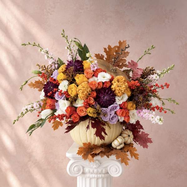 Colorful floral arrangement in a pumpkin vase with autumn leaves