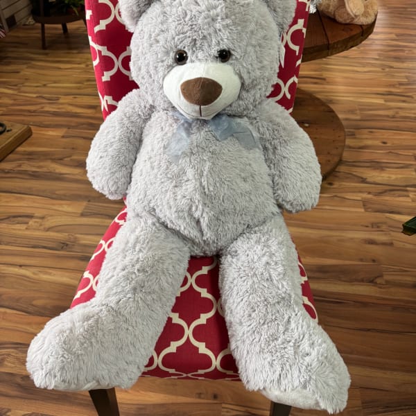 Large gray teddy bear with a ribbon bow sitting on a patterned chair