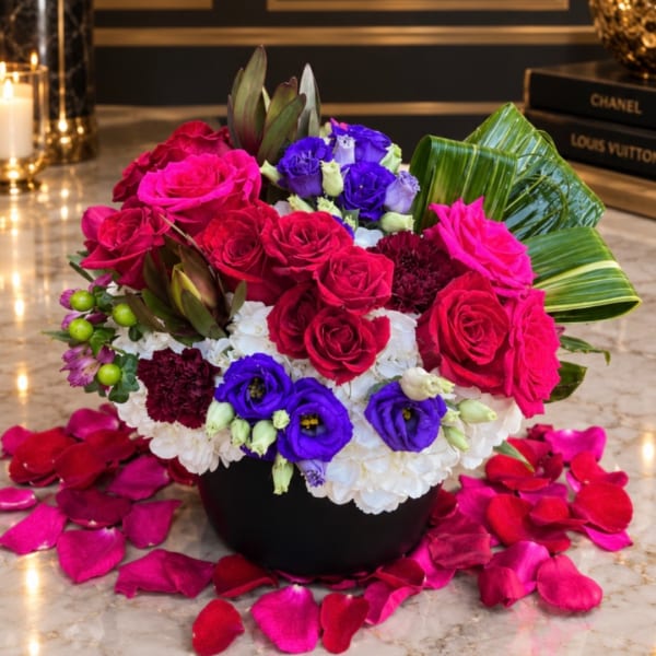 Mixed bouquet of red and pink roses with purple blooms in a black vase