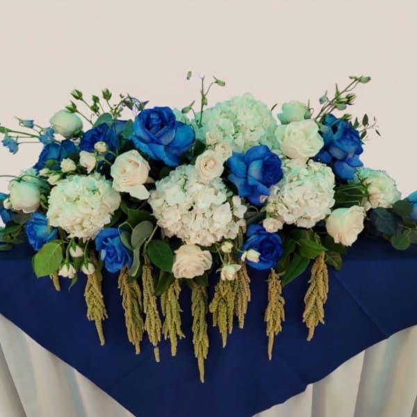 Blue and white floral arrangement with roses and hydrangeas on a draped table