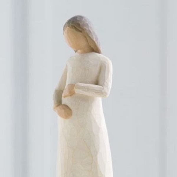 Carved wooden figurine of a woman in a long cream dress holding her belly