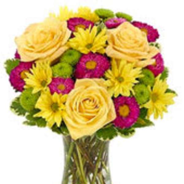 Mixed bouquet of yellow roses, yellow daisies, and pink and green mums in a clear glass vase