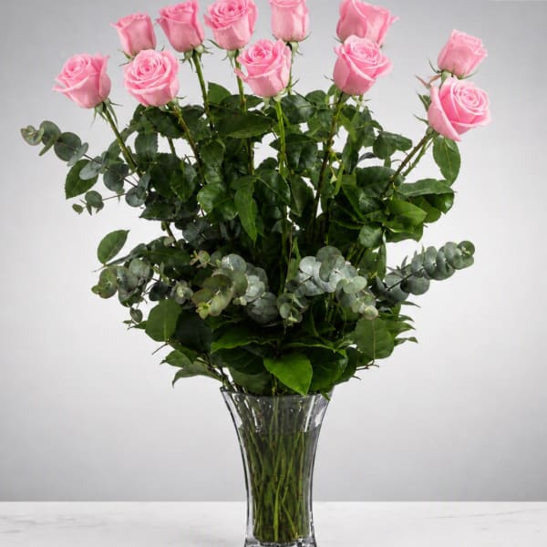 Pink roses arranged in a clear glass vase with mixed greenery