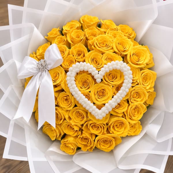 Bouquet of yellow roses wrapped in white paper with a white heart decoration