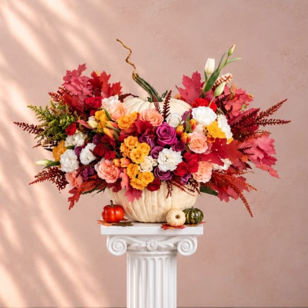 Colorful flower arrangement in a white pumpkin container with small pumpkins