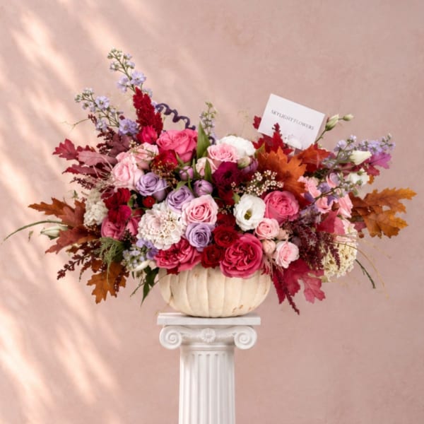 Large mixed bouquet in a cream pumpkin vase with pink, purple, and red flowers