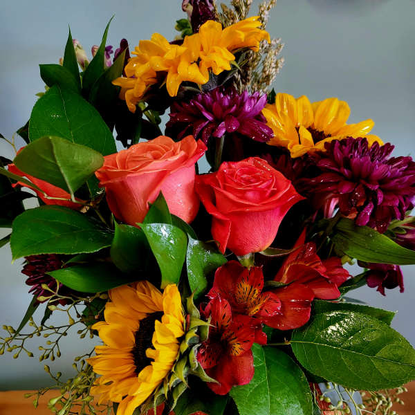 Bouquet of sunflowers, roses, and red alstroemeria with an orange ribbon