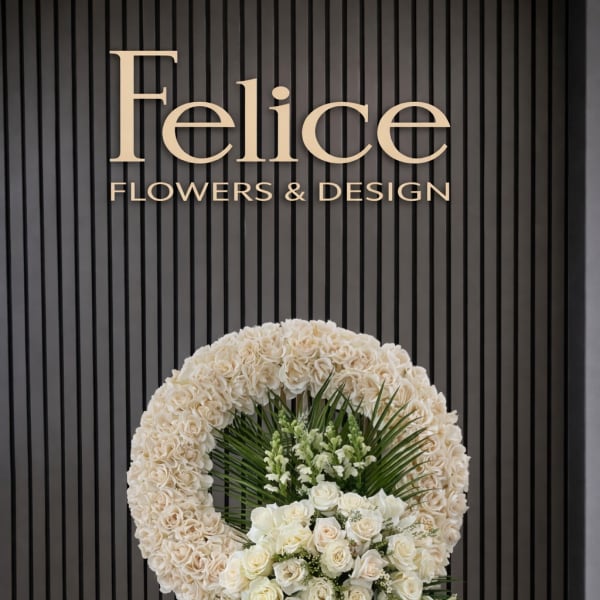 White floral standing wreath on an easel with roses and greenery