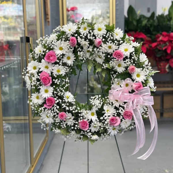 Pink roses and white daisies arranged in a circular wreath with a pink ribbon