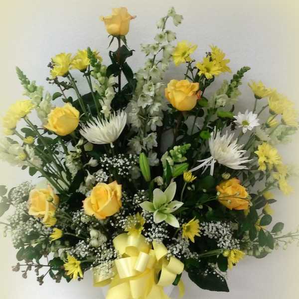 Yellow roses and white flowers arranged in a vase with a yellow ribbon