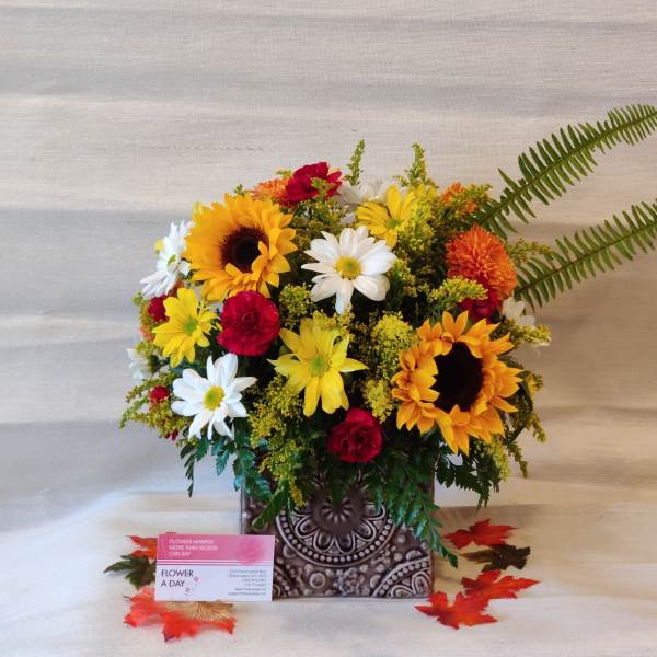 Mixed bouquet with sunflowers, daisies, and red carnations in a patterned vase