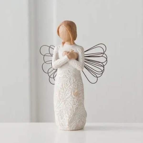 Carved angel figurine in white dress with metal wire wings holding a small heart to its chest