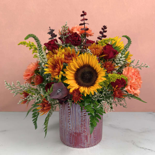 Mixed bouquet with sunflowers, red roses, and peach carnations in a pink vase