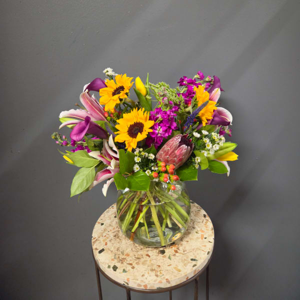 Mixed bouquet with sunflowers, lilies, and purple flowers in a glass vase