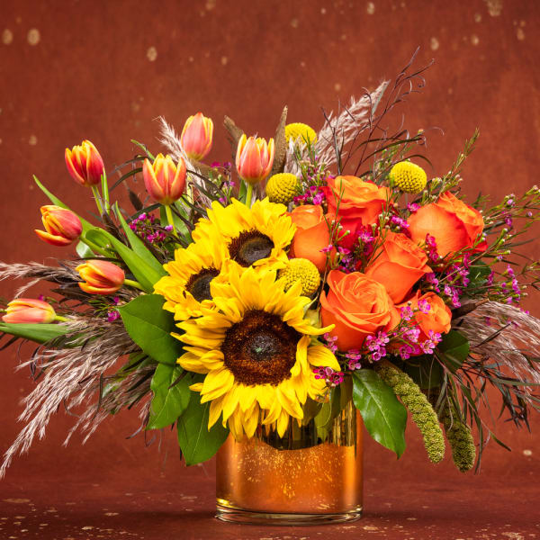 Sunflowers, orange roses, and tulips arranged in a gold vase