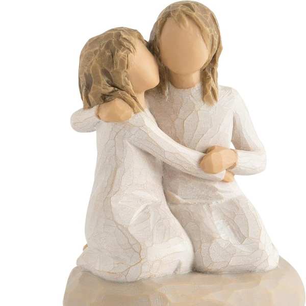 Two faceless figurines embracing in white dresses on a beige base
