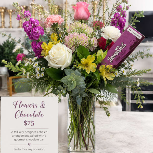 Tall mixed flower arrangement in a clear glass vase with a chocolate bar