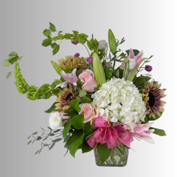 Mixed bouquet in a clear glass vase with pink lilies, roses, and white hydrangea