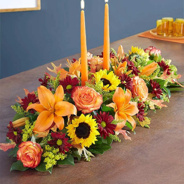 Low floral centerpiece with orange lilies, roses, sunflowers, and two orange taper candles