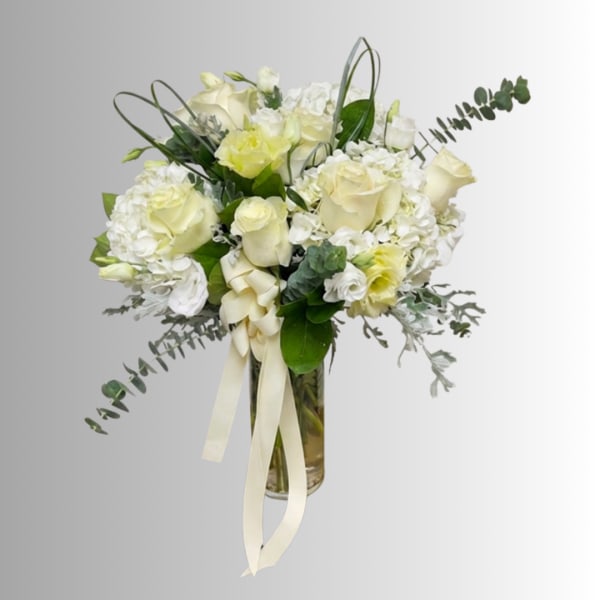 White roses and hydrangeas in a glass vase with a cream ribbon