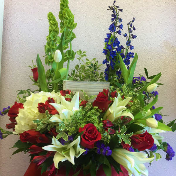 Large mixed floral arrangement with red roses, white lilies, and blue delphinium