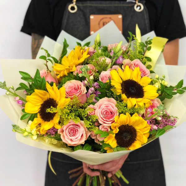 Handheld bouquet of pink roses and yellow sunflowers wrapped in pale paper