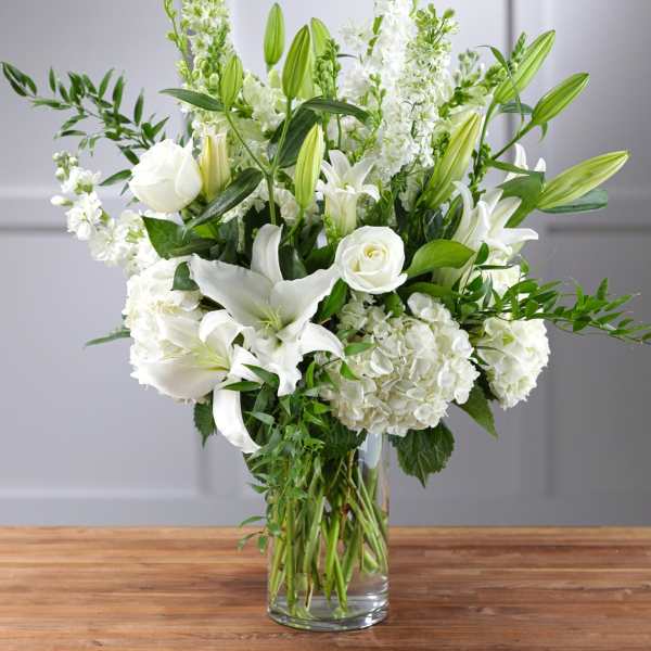 White lilies, roses, and hydrangeas in a clear glass vase