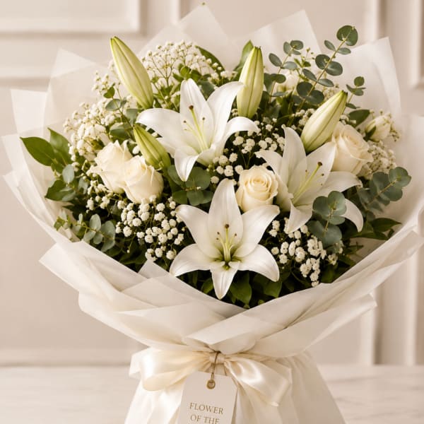 White lilies and roses arranged in a wrapped bouquet with cream ribbon.