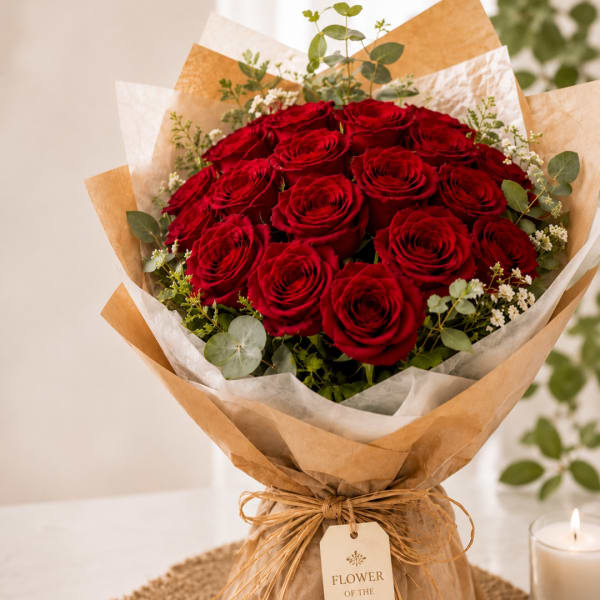 Bouquet of red roses wrapped in brown paper with a candle nearby