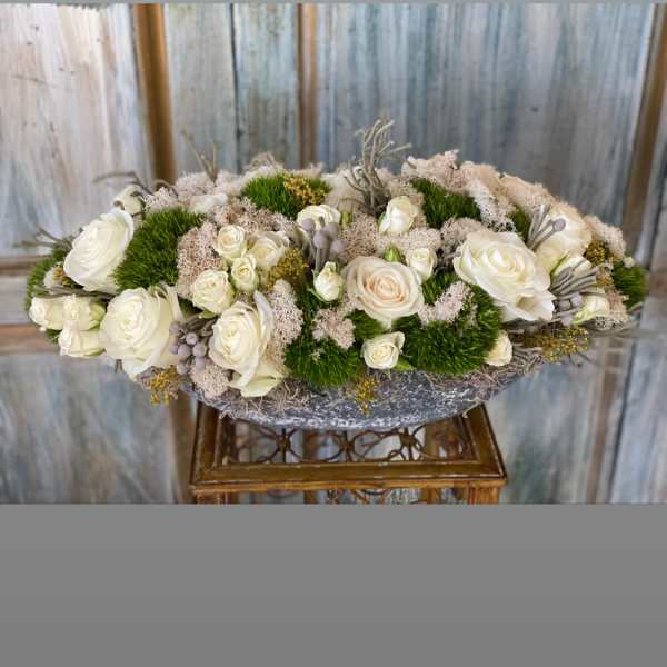 Low oval arrangement of white roses with green moss accents
