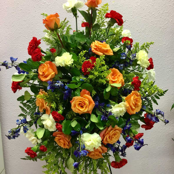 Large standing floral spray with orange roses, red carnations, and white blooms