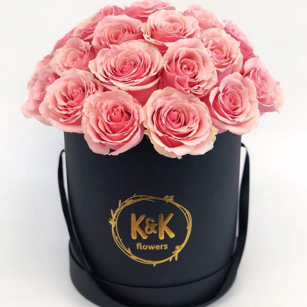 Pink roses arranged in a black round box with a gold logo