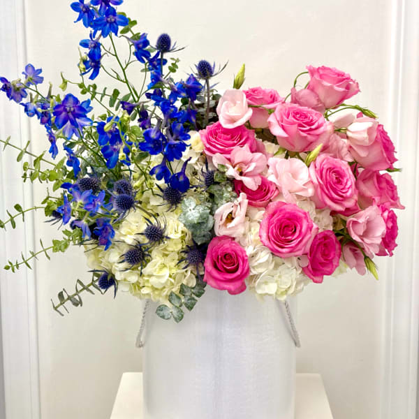 Pink roses and blue flowers arranged in a white vase