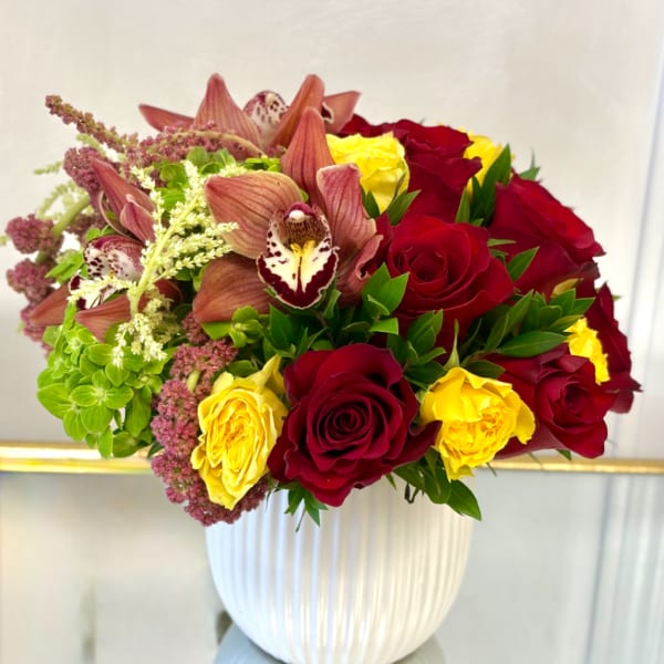 Bouquet of red and yellow roses with orchids in a white vase