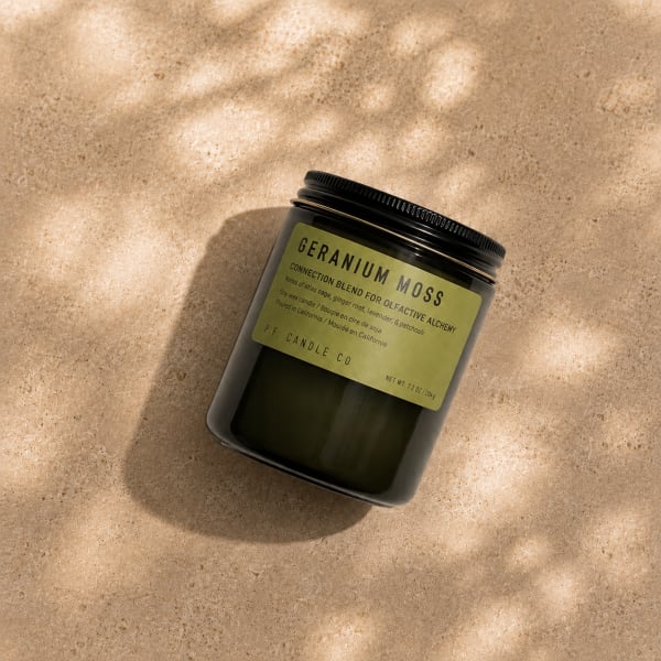 Black jar candle with a green label on a beige surface
