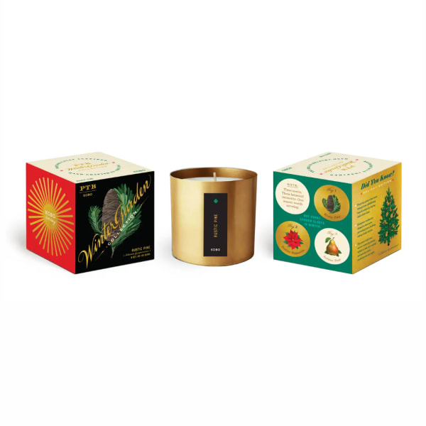 Gold candle in a metal tin between two decorative product boxes
