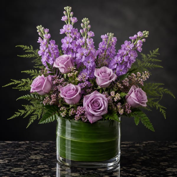 Lavender roses and purple flowers arranged in a glass vase