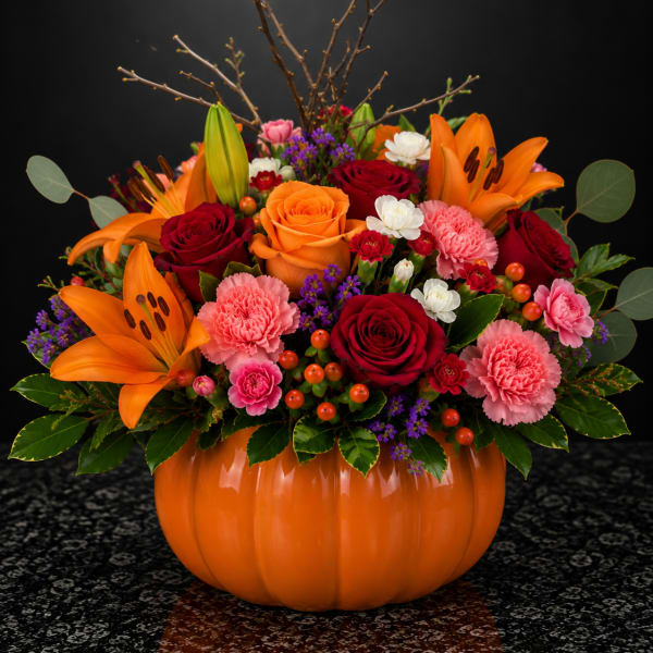 Orange lilies and red roses arranged in a pumpkin-shaped vase