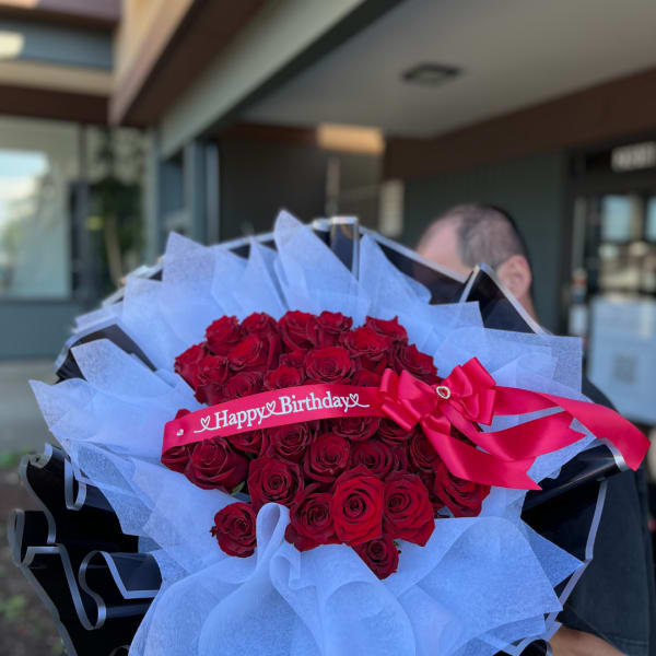 Bouquet of red roses wrapped in white paper with a pink birthday ribbon