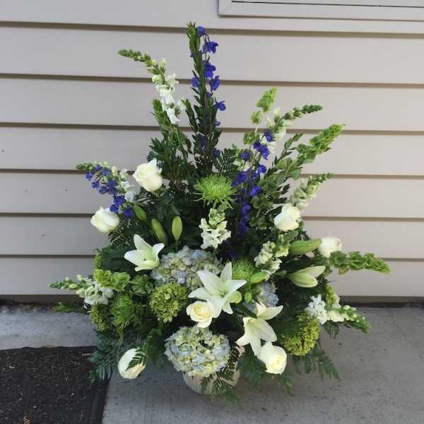 Tall floral arrangement with white lilies, roses, blue flowers, and green accents