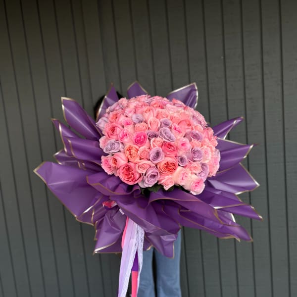 Large bouquet of pink and lavender roses wrapped in purple paper