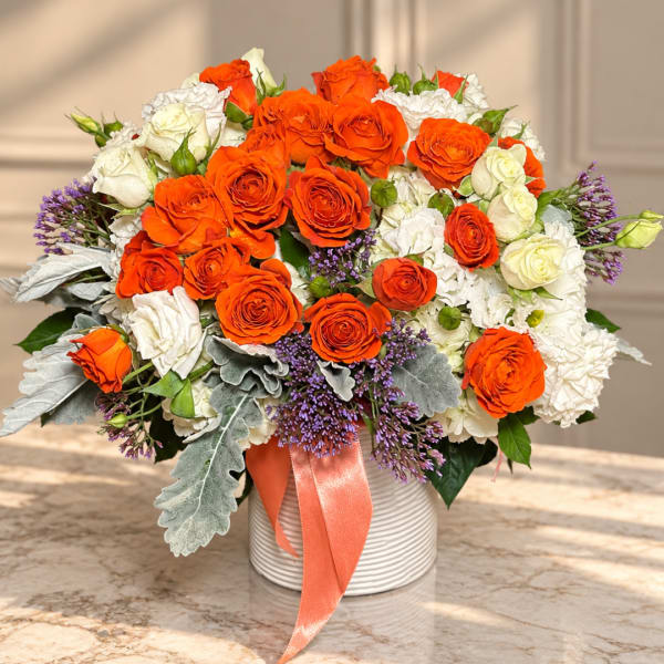 Orange and white rose bouquet in a ribbed vase with a peach ribbon