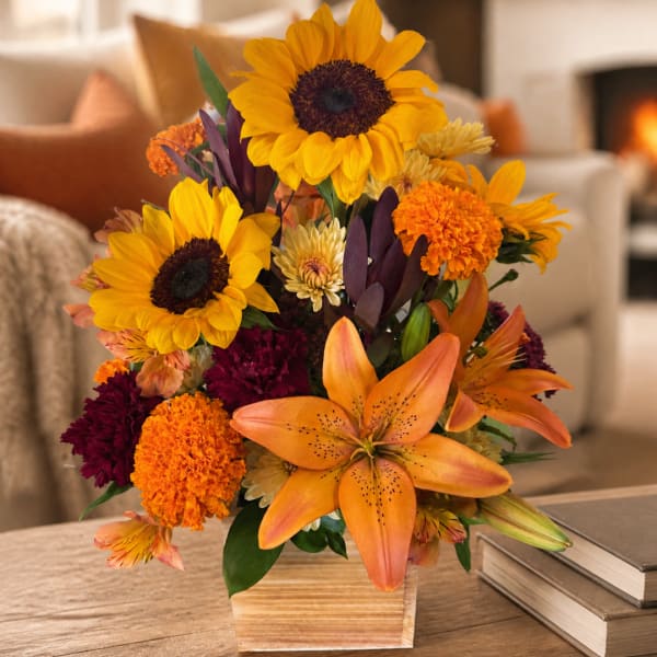Sunflowers, orange lilies, and marigolds arranged in a square vase